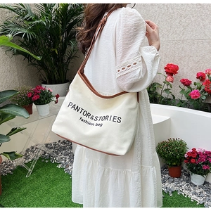 Detailed shot of large white canvas tote bag with brown leather trim and fashion logo