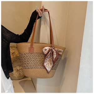 Detail of woven straw tote bag with leather handles and decorative floral silk scarf