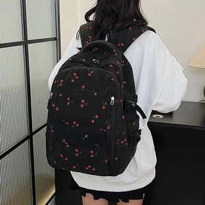 Détail d'un sac à dos en velours côtelé noir avec motifs cerises et sangles de côté utiles