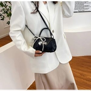 Detail of black mini PU leather crossbody bag featuring pearl bow and heart pendant charm