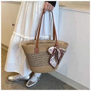 Detail of woven straw tote bag with brown leather handles and floral silk scarf accessory