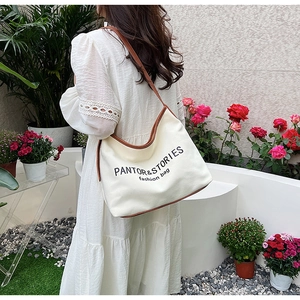 Outdoor shot of a white canvas tote bag with brown leather trim worn by a model
