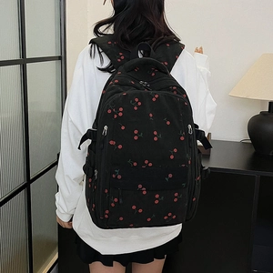 Gros plan d'un sac à dos en velours noir avec motifs cerises et détails de zip