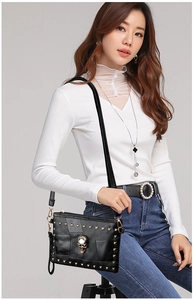 Detail of black textured leather crossbody bag with golden skull and rivet decorations