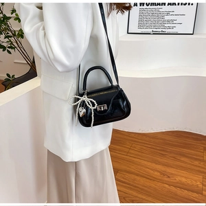 Close-up of black glossy PU leather mini bag with pearl bow and silver heart pendant