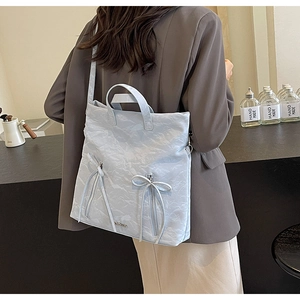 Detail view of light blue textured tote bag with bow zippers worn by a model