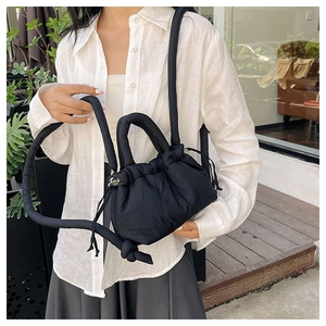 Fashionable black quilted puffer shoulder bag styled on model in bright casual outdoor setting