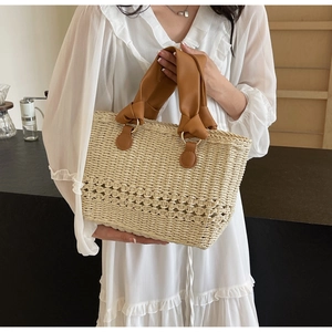 Detailed view of the woven straw texture and stylish knotted brown leather handle