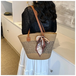 Detail of hand-woven straw tote bag with brown leather straps and floral silk scarf accessory