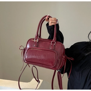 Detailed close-up of glossy burgundy PU leather handbag with ribbons and detachable strap