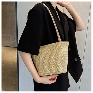 Close-up of a handwoven straw shoulder bag with leather straps on a model with blazer