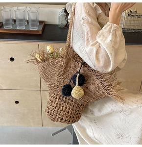 Dettaglio della borsa tote in paglia intrecciata con pompon decorativi e frange