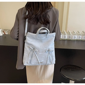 Detail of light blue PU leather backpack featuring zipper bows and gold logo