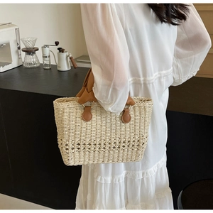 Detail of straw woven tote bag with hollow patterns and brown leather handles in a cafe