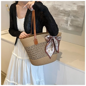 Detail of woven straw tote bag with brown leather handles and a decorative silk scarf