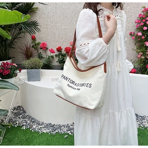 Detail of canvas shoulder bag with brown leather trim and fashion text print