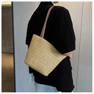 Close-up of beige woven straw tote bag with brown leather straps on a model's shoulder