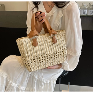 Detail of woven straw handbag featuring hollow diamond patterns and brown knotted leather handles