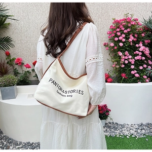 Minimalist canvas crossbody bag with brown leather trim shown in a garden setting