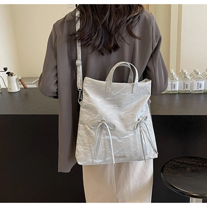 Light grey PU leather shoulder bag with bow details and vertical zippers on a model