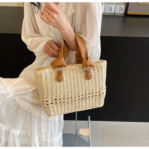 Close-up of woven straw tote bag with knotted brown leather handle and gold hardware