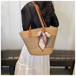 Detailed macro view of woven straw tote bag with a floral scarf on brown leather strap
