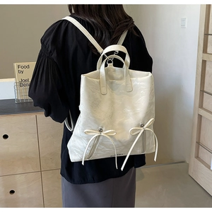 Detail of off-white PU leather backpack featuring bow decorations and vertical zippers