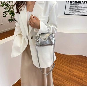 Detail of silver metallic crossbody bag with pearl chain and heart charm on white blazer