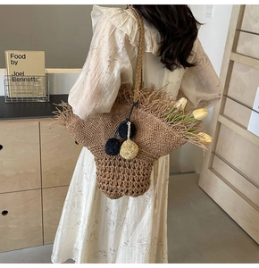 Dettaglio della borsa tote in paglia fatta a mano con frange decorative e ciondolo a pompon