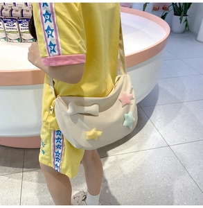 Détail du sac croissant en nylon beige avec étoiles en peluche et pendentif os