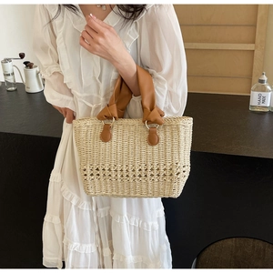 Detail of straw handbag with brown leather handles held by a model in a white dress