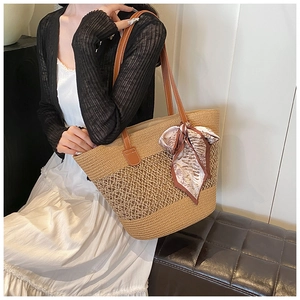 Detail of hand-woven straw tote bag with brown leather handles and silk scarf decoration