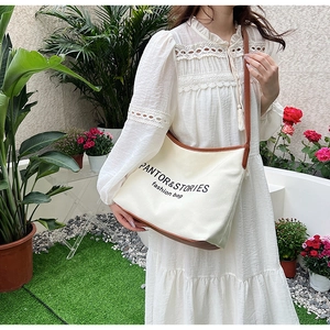 Detail of canvas shoulder bag with brown leather trim and PANTOR & STORIES print text