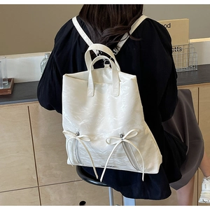 Detail view of white PU leather backpack with ribbon bows and pleated texture shown on model