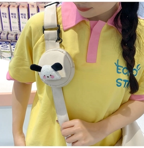 Détail d'une mini pochette ronde en nylon beige avec un charm de chien en peluche sur la sangle