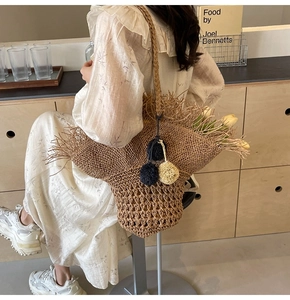 Dettaglio di borsa in paglia con bordi sfrangiati in rafia e ciondoli a pompon colorati
