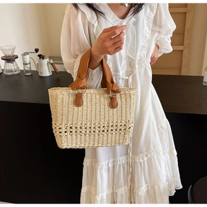 Close-up of woven straw handbag featuring a brown leather handle with knot detail