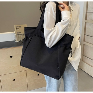 Detail shot of black nylon tote bag with drawstring side and branded logo label