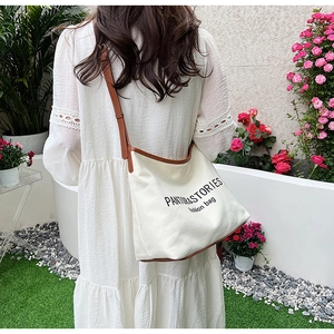 Detail of canvas hobo bag with brown leather trim worn by model in a garden