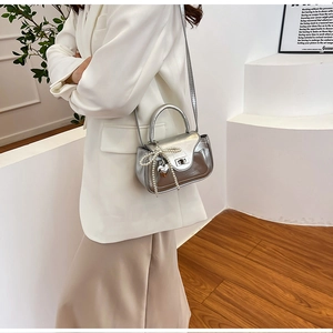 Detail of silver PU leather crossbody bag with pearl bow and metal heart charm on model