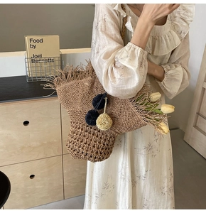 Dettaglio della borsa in paglia intrecciata con bordo sfrangiato e pompon decorativi