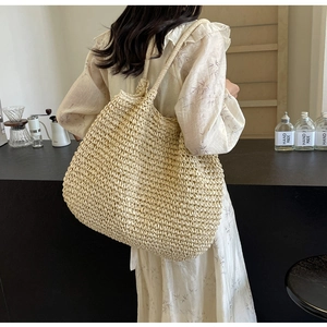 Detail of a large woven tote bag in beige crochet texture worn by a model in a café setting