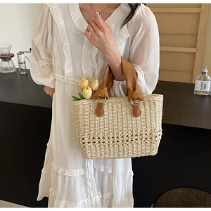 Detail of woven straw handbag with brown leather handles and decorative knots