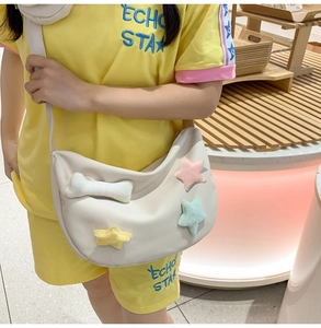 Détail du sac bandoulière en nylon beige avec étoiles en peluche et pendentifs en os