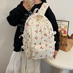 Détail d'un sac à dos en velours côtelé crème avec imprimé cerises et poches à boucles