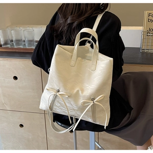 Detail of white PU backpack featuring polished pleated texture and bow zipper accents