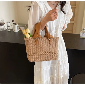 Detail view of woven straw tote bag featuring hollow floral pattern and brown leather handles