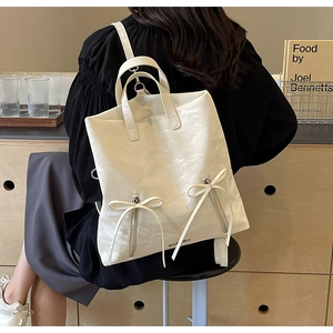 Detail of white PU leather backpack featuring bow-ribbon zippers and pleated texture