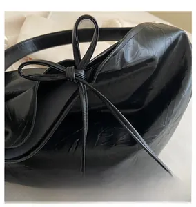 Detailed macro shot of a black glossy pleated PU leather handbag with a chic ribbon bow