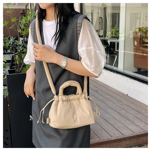 Close-up of beige drawstring bucket bag featuring pleated fabric and round handle design